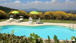 Ein Poolbereich mit Liegestühlen und Sonnenschirmen, umgeben von einem Zaun und mit Blick auf die Landschaft.