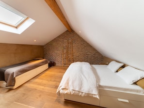 A loft bedroom with a sloped ceiling, exposed brick wall, wooden beams, a loft bed, and a window. - Bertrix Charming 2-bedroom Holiday Home (Bertrix)