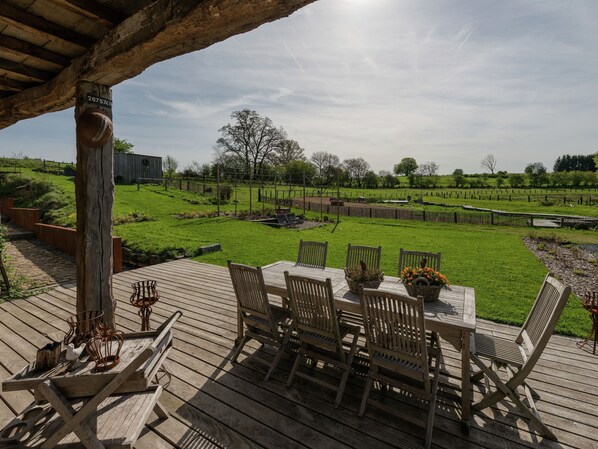 A wooden deck with a table and chairs, overlooking a grassy area with a fence and trees.