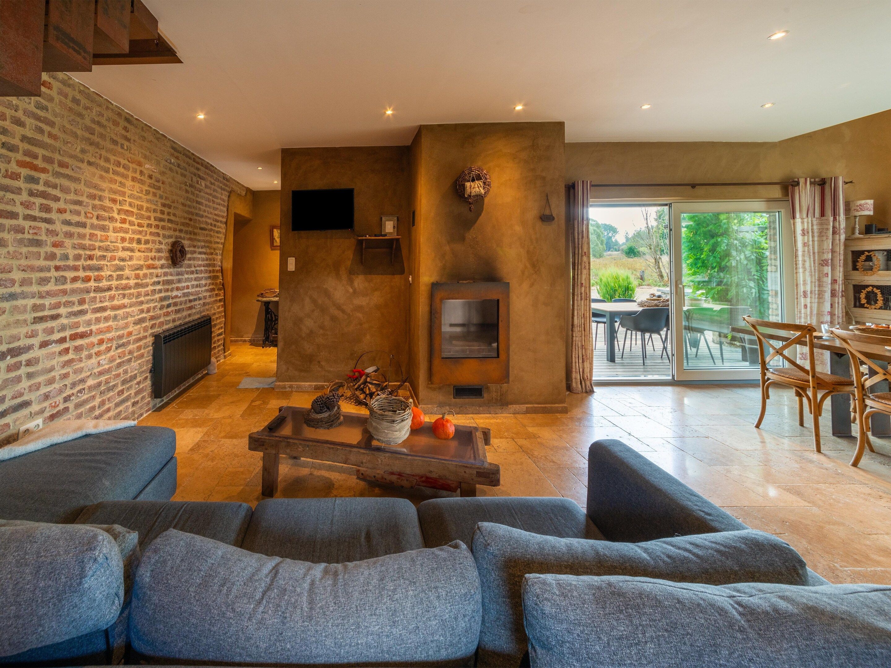 A modern living room with a brick wall, a fireplace, and a dining area with outdoor view.