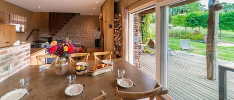 A dining area with a brick wall, wooden chairs, a table set with plates, glasses, and a fruit basket.