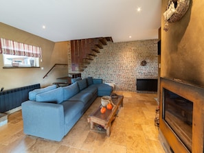 A modern living room with a sectional sofa, a fireplace, a brick wall, and a staircase. - Bertrix Charming 2-bedroom Holiday Home (Bertrix)