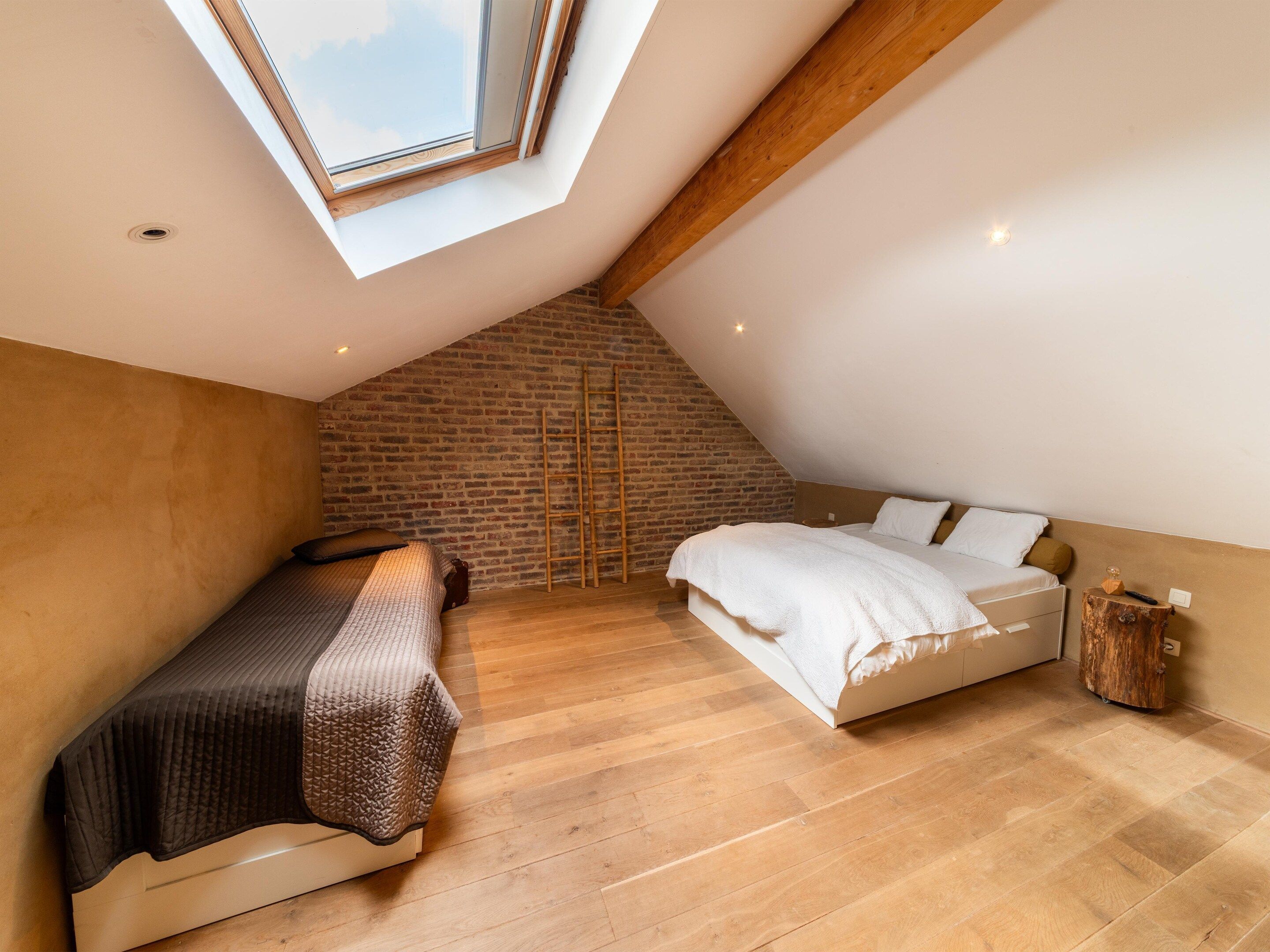 A loft bedroom with a sloped ceiling, exposed brick wall, and a skylight.