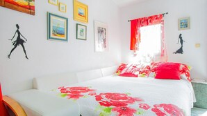 A bedroom with a bed, a white couch, and a window with red curtains. - Refreshing Apartment in Omis With Balcony (Omis)
