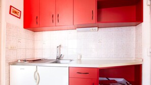 A kitchen with red cabinets, a white countertop, a built-in dishwasher, and a tiled backsplash. - Refreshing Apartment in Omis With Balcony (Omis)