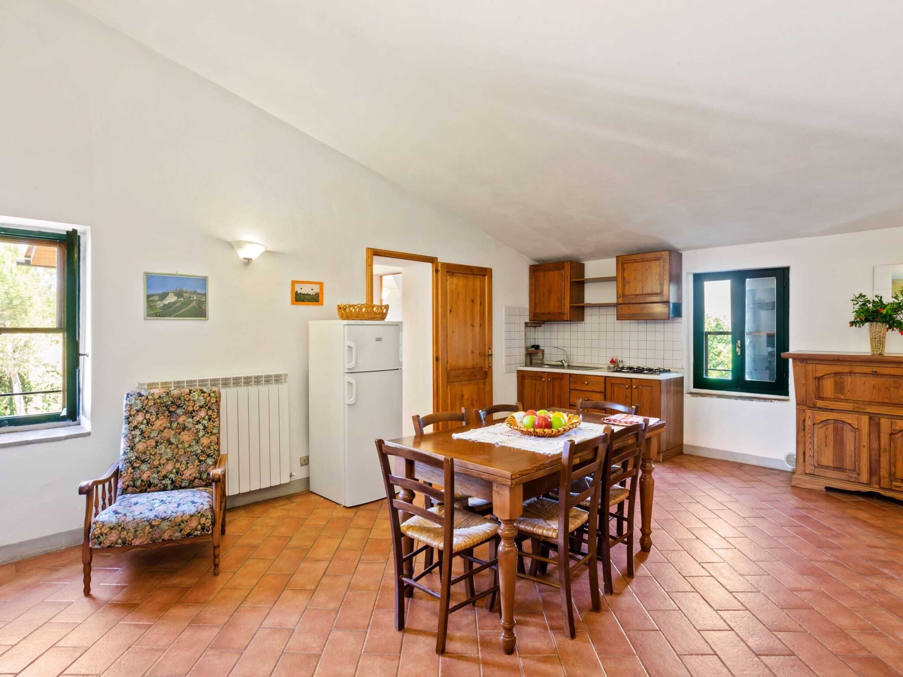 Uma sala de jantar com mesa e cadeiras de madeira, uma geladeira e uma janela com vista para o verde.