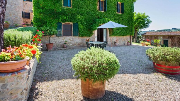 A stone building with a green ivy-covered exterior, a gravel courtyard, and potted plants. - Escape Near San Gimignano (San Gimignano)