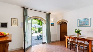 A dining area with a table and chairs, a basket of fruit, and a view through an open door to an outdoor patio. - Escape Near San Gimignano (San Gimignano)