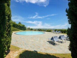 Una piscina con solárium de piedra, rodeada de vegetación y un cielo despejado.