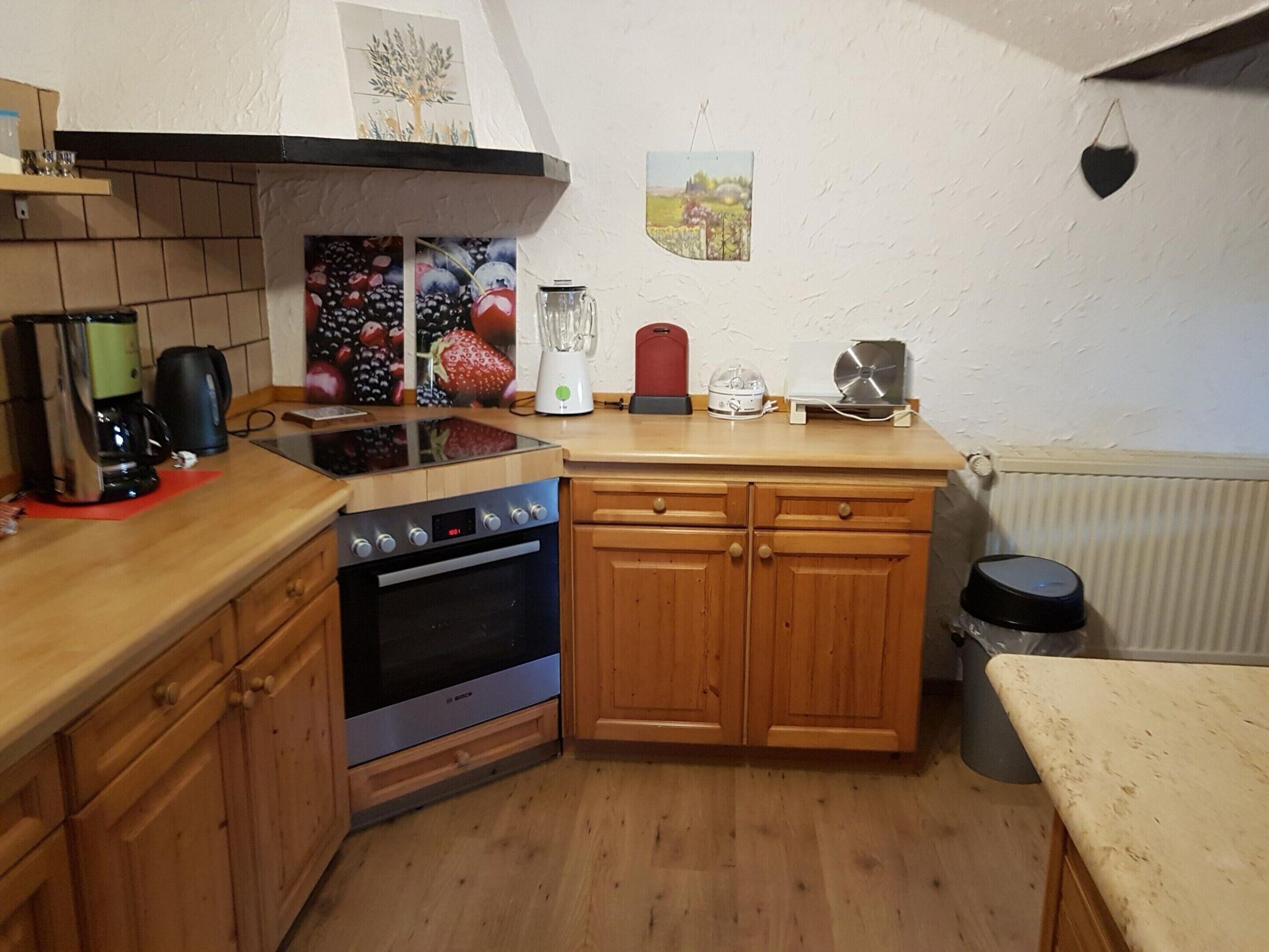 A compact kitchen with wooden cabinets, a Bosch oven, a coffee maker, and a blender on the countertop.