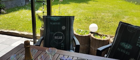 Un patio con una mesa lista para dos personas, con una botella de champagne Duval-Leroy, dos copas de vino, un florero y una jarra de cerámica verde.