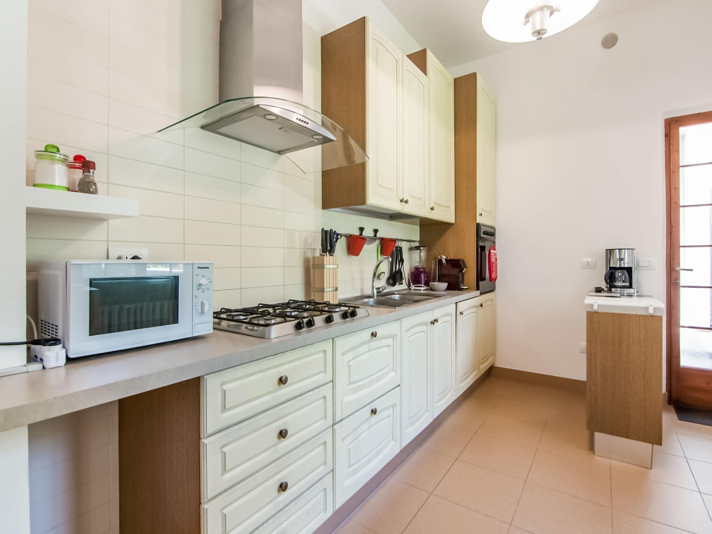 Una cucina con mobili bianchi, un fornello a gas, un forno a microonde e una macchina per il caffè.