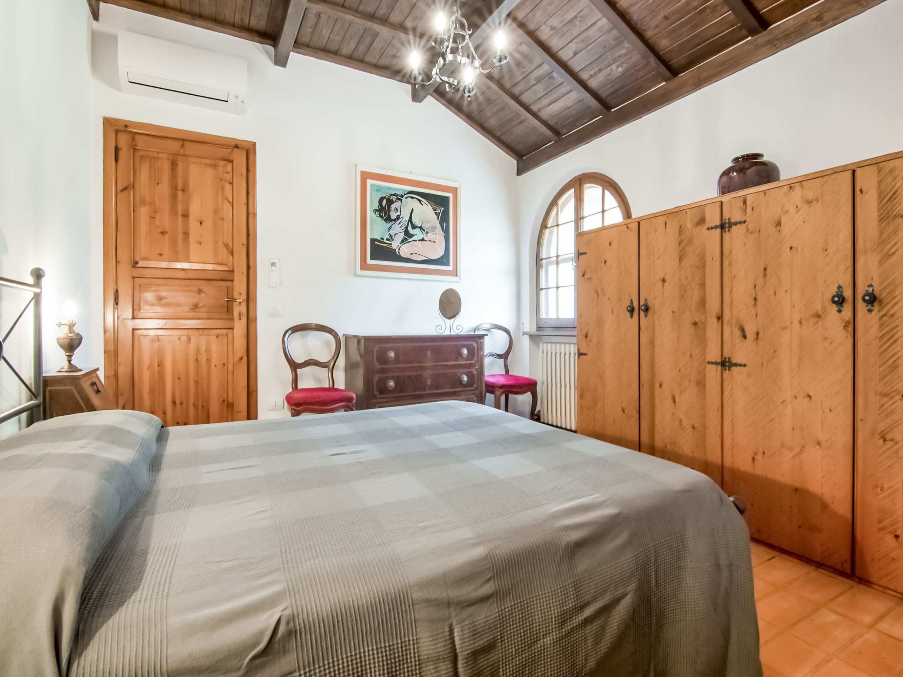 A bedroom with a large bed, wooden wardrobe, and a painting on the wall.