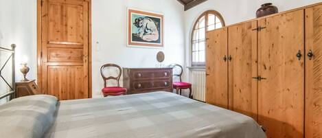 A bedroom with a large bed, wooden wardrobe, and a painting on the wall.