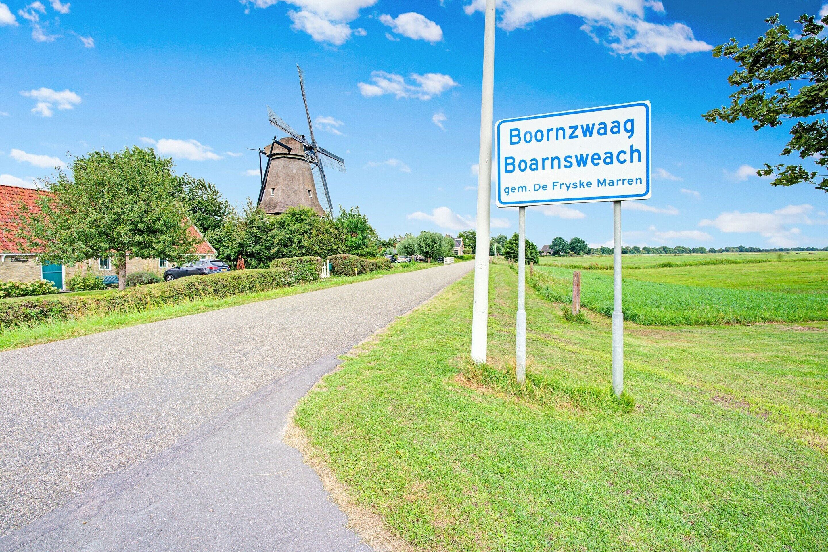 A rural road with a windmill in the background and a sign indicating Boornzwaag Boornsweach.