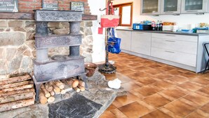 Une cuisine avec une cheminée en pierre, une étagère en bois ornée d’enseignes et un sol carrelé.