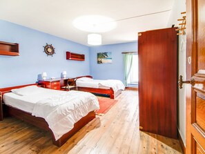 A hotel room with two wooden beds, a desk, a chair, a desk lamp, a wall clock, and a painting.
