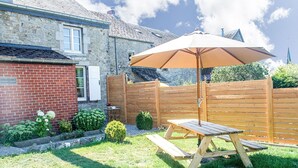 Een houten picknicktafel met een zonnescherm in een achtertuin, met een stenen muur, een bakstenen huis en een houten omheining.