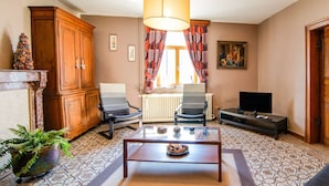 Een woonkamer met een open haard, een televisie, een salontafel en vloertegels met een patroon.
