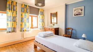 Een slaapkamer met een houten bed, een dressoir, een stoel, een spiegel en een raam met gordijnen.