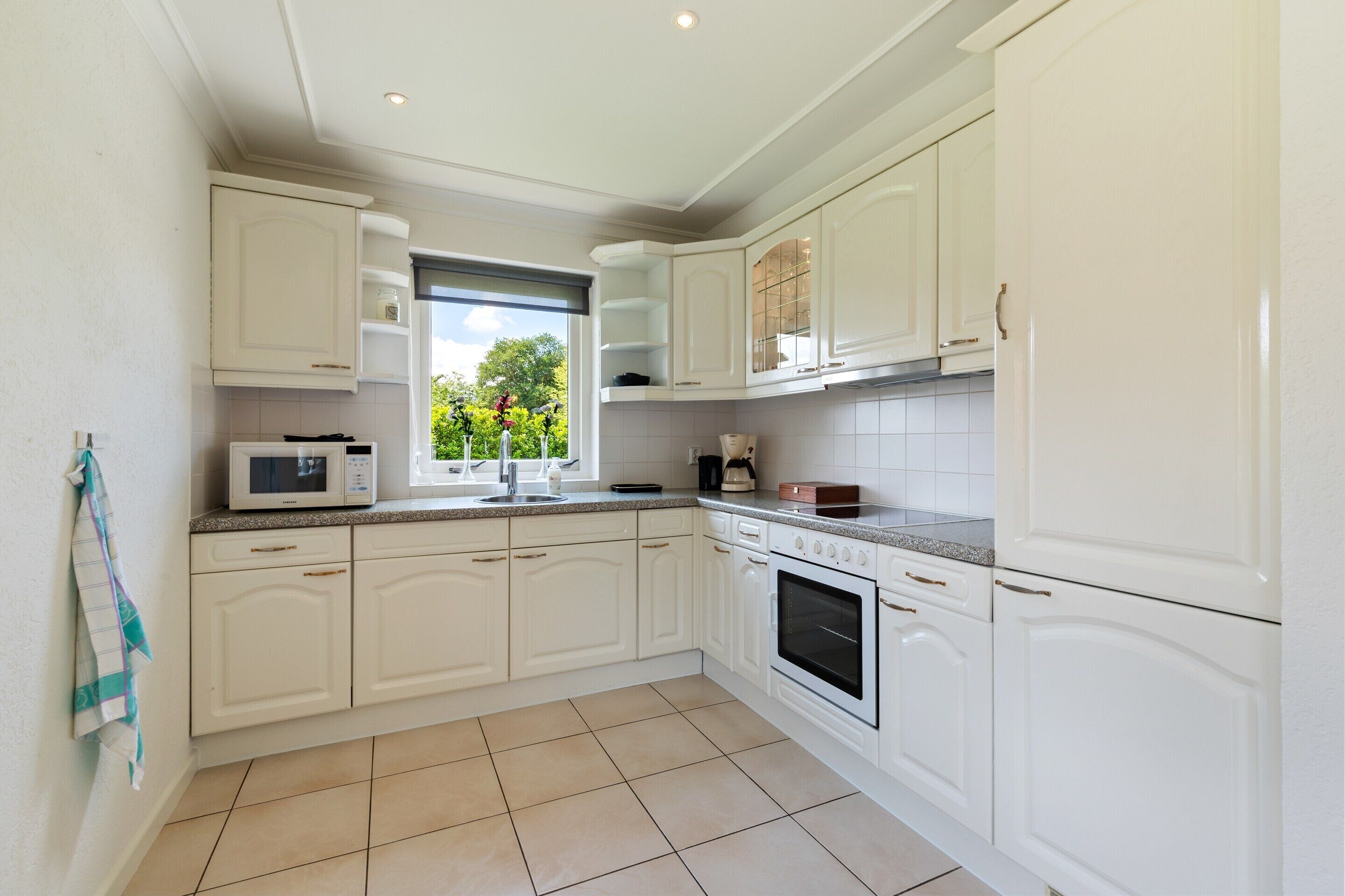 A modern kitchen with white cabinetry, a microwave, a stove, and a window with a view of greenery.