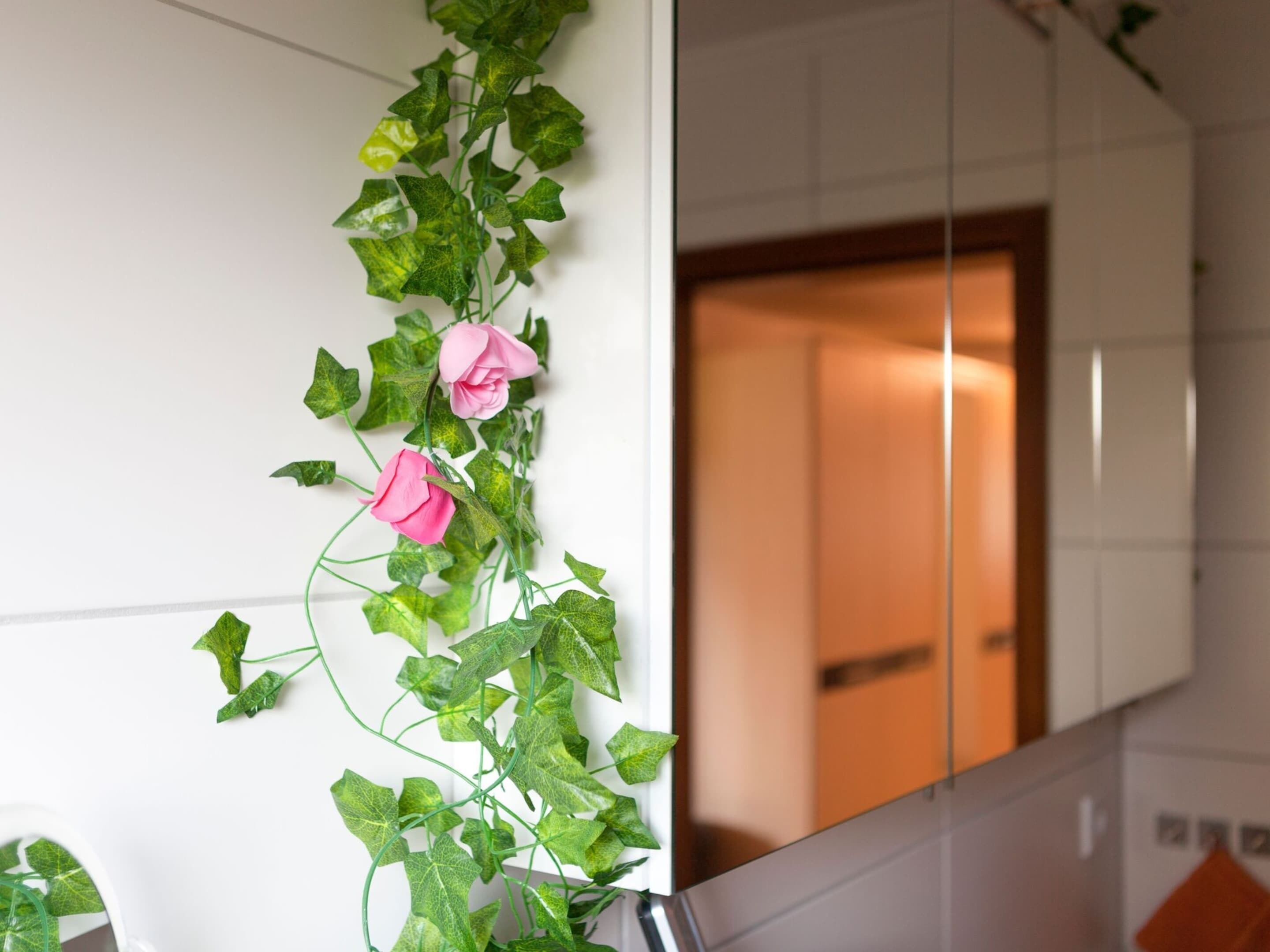 Una pared cubierta por una planta trepadora con hojas verdes y flores rosadas.
