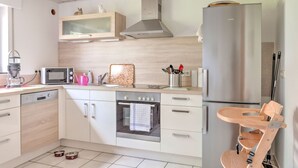 Una cocina moderna con microondas, horno y refrigerador integrados. Hay una silla de madera y un comedero para mascotas.