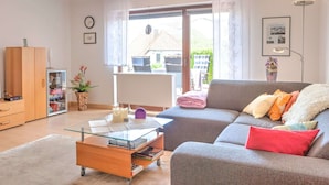 Una sala de estar moderna con un sofá gris, una mesa de centro de cristal y un armario de madera.