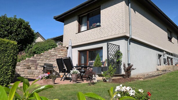 Una casa de dos pisos con una escalera de piedra que conduce a la entrada, un patio con mobiliario exterior y un jardín bien cuidado.