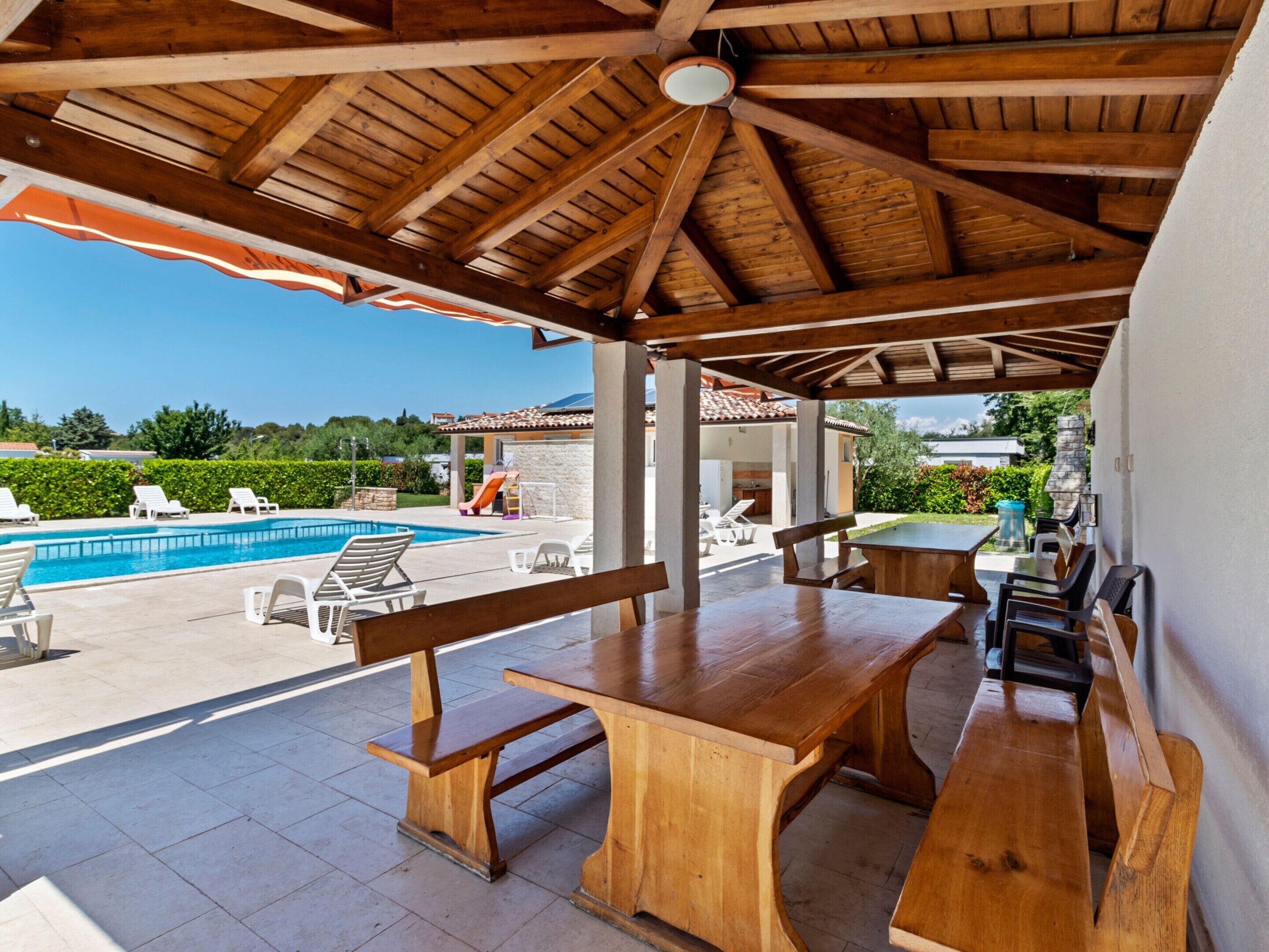 Un patio al aire libre con bancos y mesas de madera, una piscina y vistas del paisaje circundante.