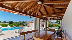 Patio esterno con panche e tavoli di legno, piscina e vista sul paesaggio circostante.