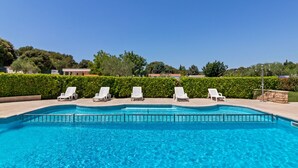 Una piscina cristallina azzurra con comode poltrone da sdraio e un siepe sullo sfondo.