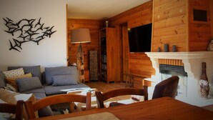 A cozy living room with a fireplace, wooden walls, a sofa, and a dining table. - Chalet Chocolat chaud 4 rooms - 90m², sleeps 7 in the heart of Belleville (st martin de Belleville)