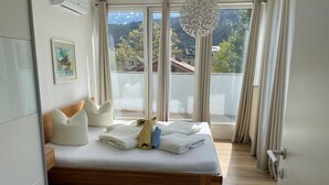 A modern bedroom with a wooden bed, white bedding, and a view of a mountain landscape through large windows. - Apartment Innsbruck Near Bergisel Ski Jump (Innsbruck)