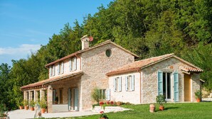 A stone house with a tiled roof, a covered porch, and a well-maintained lawn.