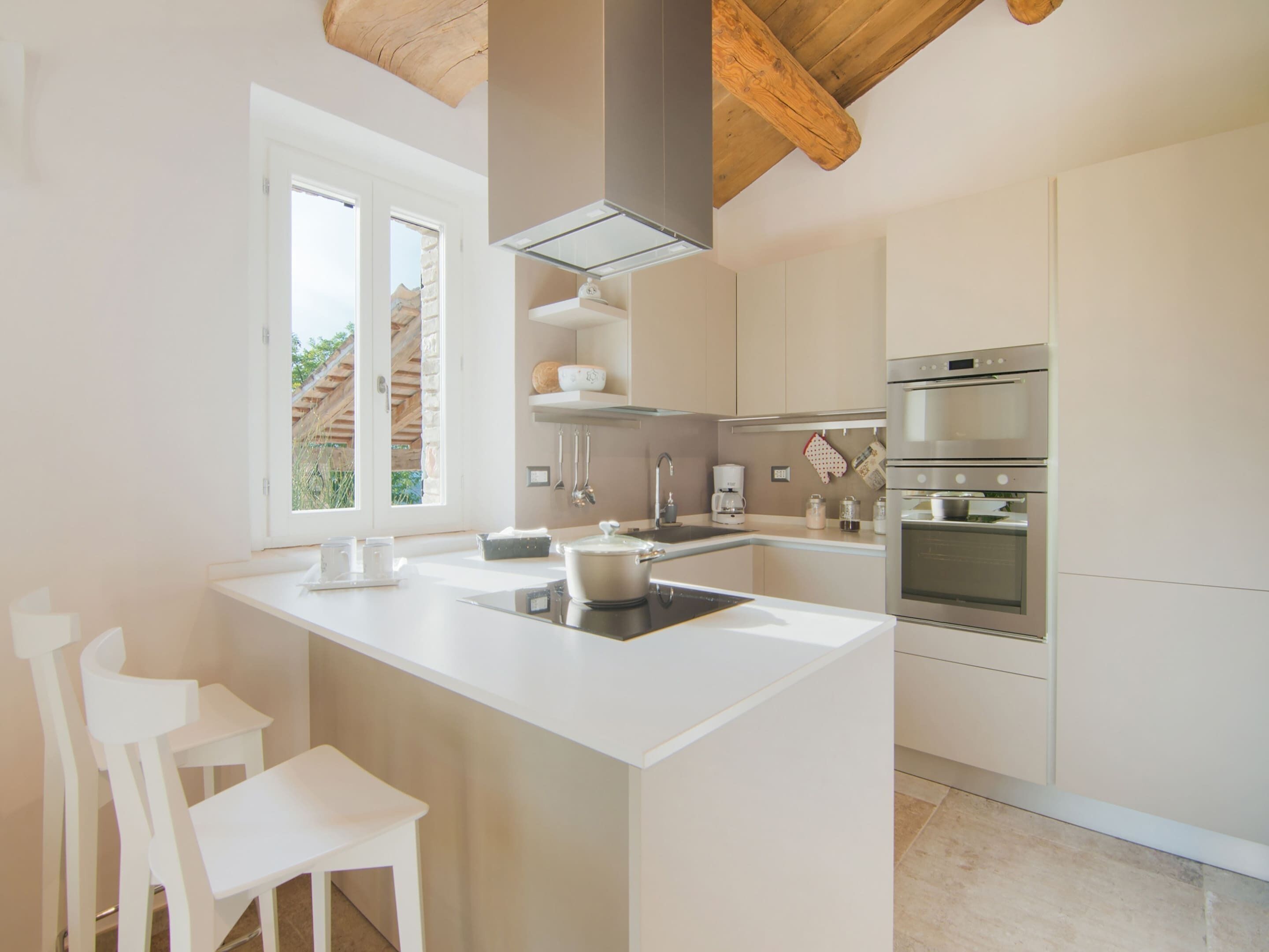 A modern kitchen with a central island, white cabinetry, and a built-in oven.