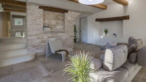 A modern living room with exposed wooden beams, a stone wall, a sofa, and a hanging light fixture.