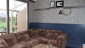 A brown upholstered sectional sofa with a wooden coffee table, a brass horn, and framed pictures on the wall. - Nice Vacation Home in Horssen With Garden (Horssen)