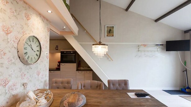 A dining area with a wooden table, chairs, a clock, and a chandelier. - Nice Vacation Home in Horssen With Garden (Horssen)