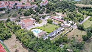 Ett flygbildsbild av ett bostadsområde med flera byggnader, en swimmingpool och omgivande grönska.