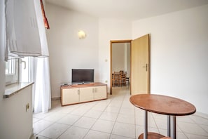 A room with a TV on a wooden cabinet, a dining table, and a door leading to another room.