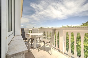 Varanda com mesa e duas cadeiras, corrimão branco e vista para área verde.