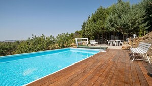 Um deck de madeira com piscina, cadeiras de descanso brancas e uma parede de pedra.