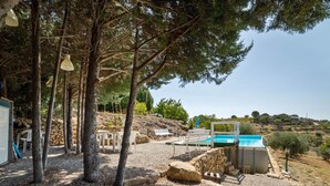 Área de piscina com parede de pedra, um banco branco e uma mesa com cadeiras.