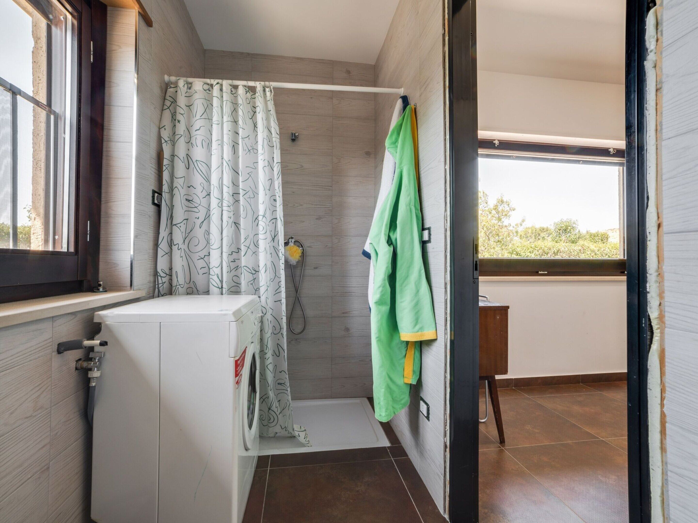 A compact bathroom with a shower, a small washing machine, and a window providing natural light.