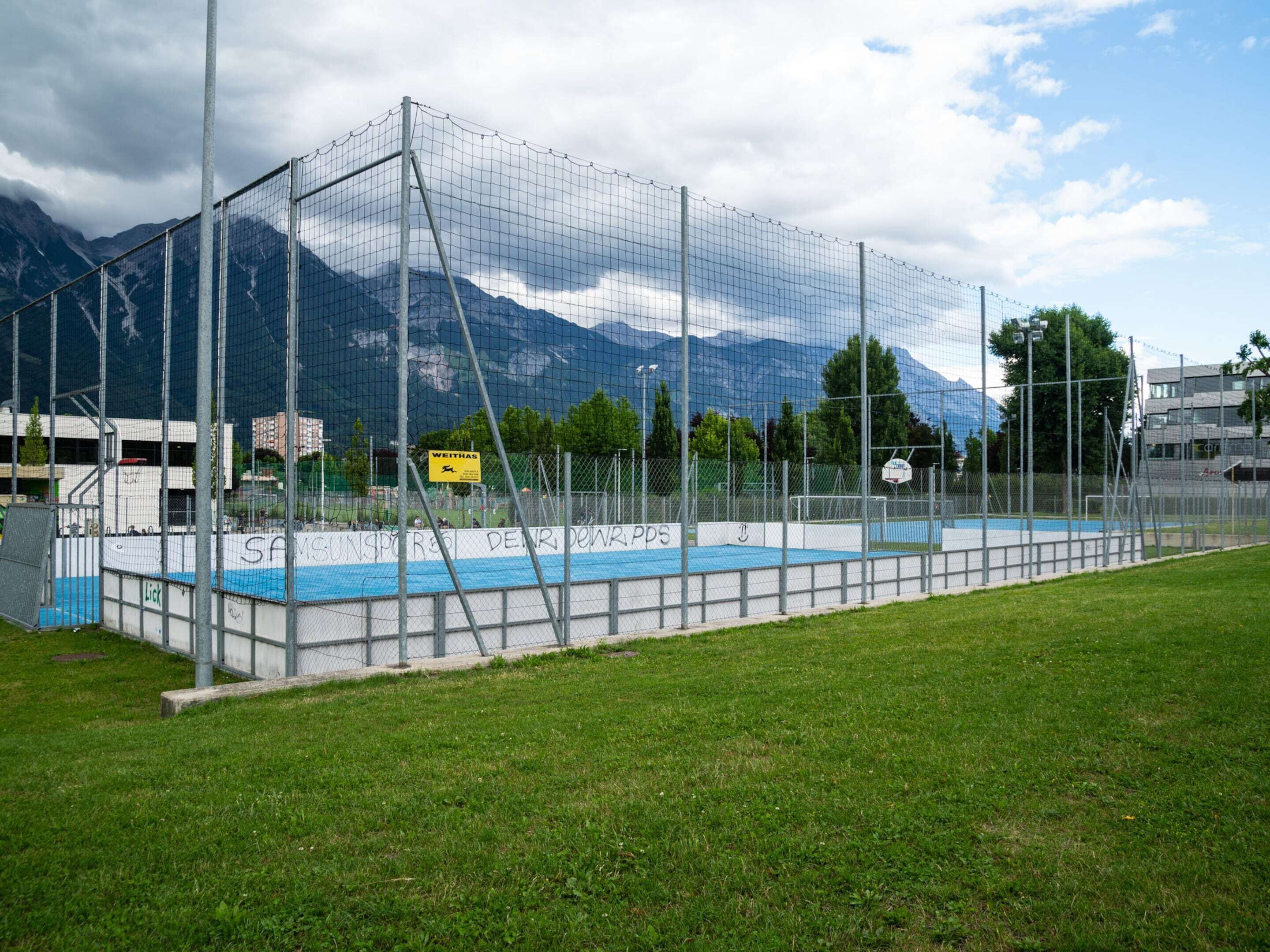 Una cancha deportiva cercada con un aro de baloncesto, con montañas al fondo.