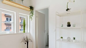 A room with a wooden floor, a black vase with dried branches, a white shelving unit with plants, and a window with a view of buildings. - Apartment Innsbruck near Bergisel Ski Jump (Innsbruck)