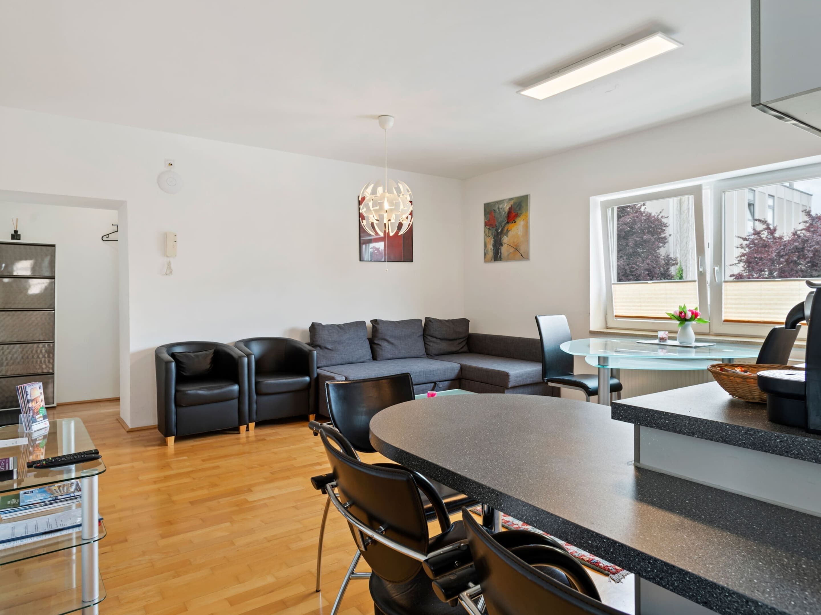 A modern living room with a sofa, chairs, a dining table, and a kitchen area.