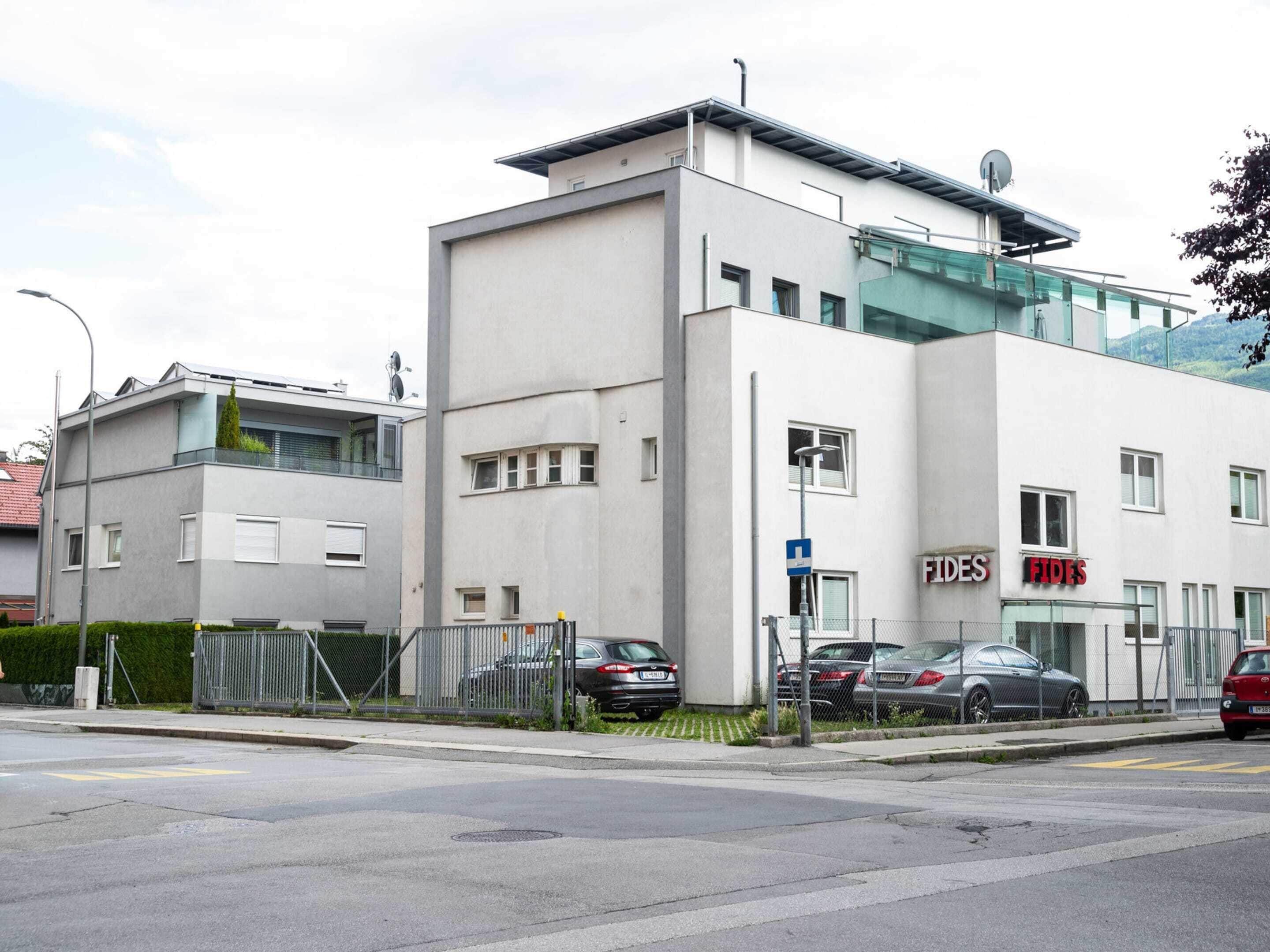 A modern building with a white facade, a glass section on the upper floor, and a sign for 'FIDES' on the right side.