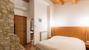 Ein Schlafzimmer mit Steinwand, Holzbalkendecke, einem Bett, einem Heizkörper und einer Holztür.